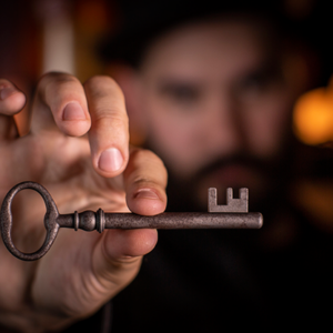 Mann im Hintergrund mit Hand die einen alten Schlüssel zwischen Daumen und Zeigefinger hält im Vordergrund