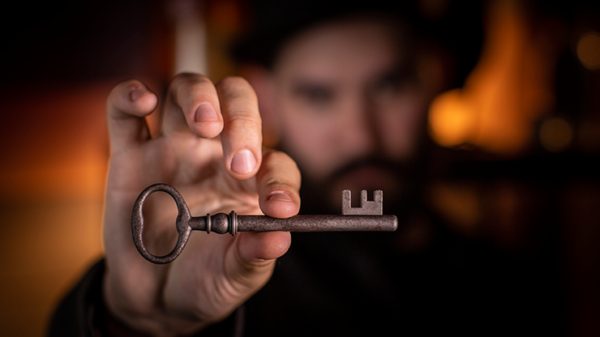 Mann im Hintergrund mit Hand die einen alten Schlüssel zwischen Daumen und Zeigefinger hält im Vordergrund
